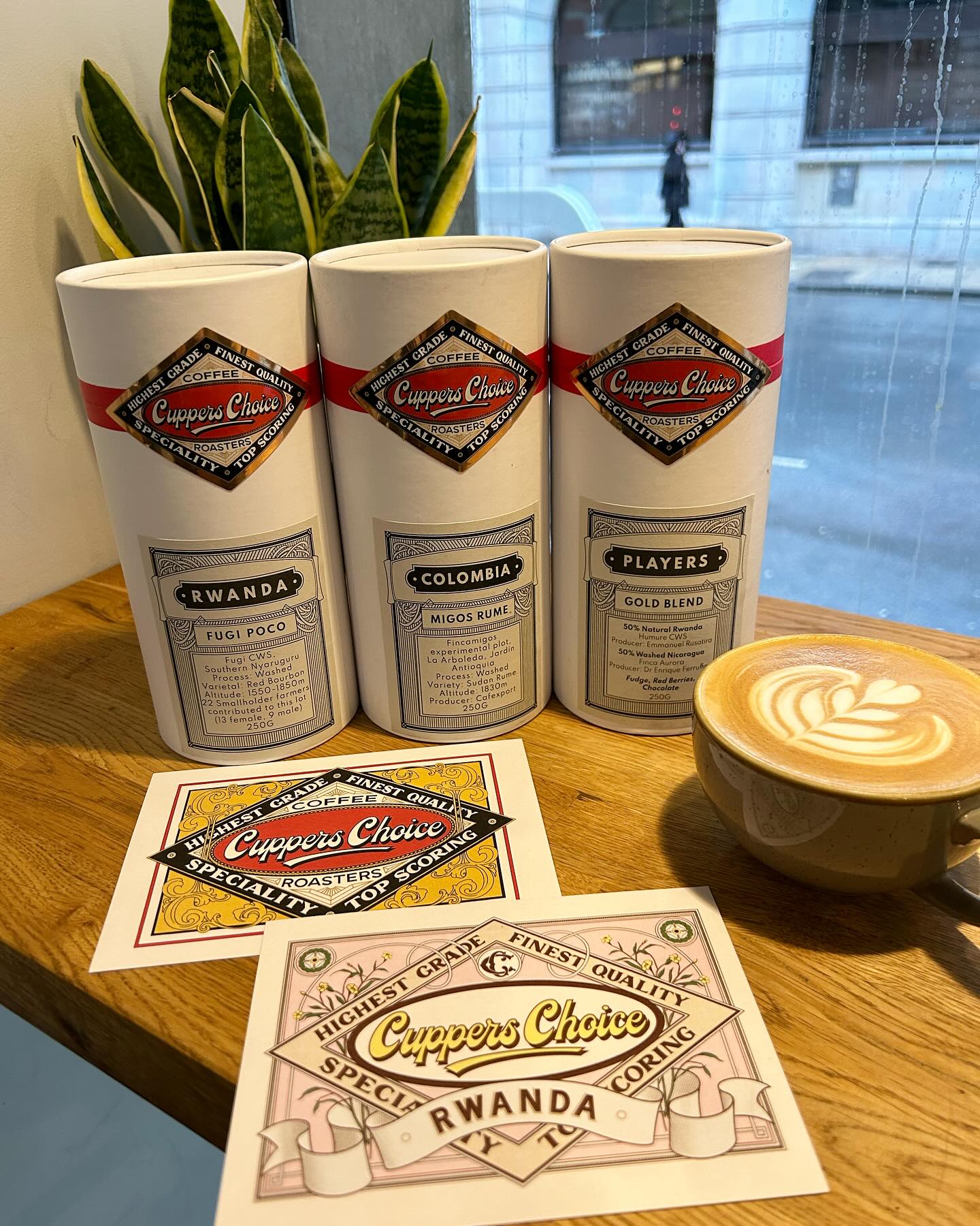 Cuppers Choice speciality coffee tins beside a flat white